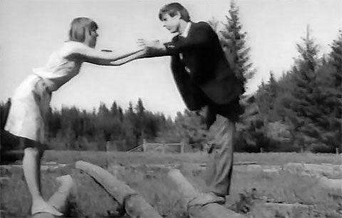 Bei einem Ausflug aufs Land stehen sich Sabine und Werner gegenüber auf zwei Baumstämmen auf einer Wiese und halten sich an den Händen