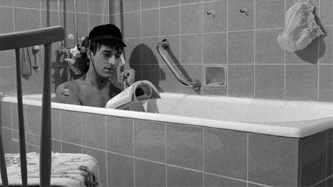 Werner Enke in der Badewanne, wo er die Badebrause als Telefonhörer zweckentfremdet verwendet, während er ein Buch liest
