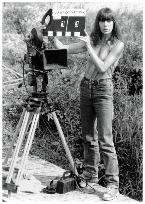 May Spils auf einem Steg neben einer analogen Filmkamera stehend mit einer Filmklappe bei Dreharbeiten zu "Aktion Schmetterling"